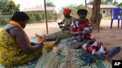 FILE— Women survivors weave grass and thread bowls outside their home at Mybo reconciliation village in Nyamata, in Kigali, Rwanda, April 5, 2024.