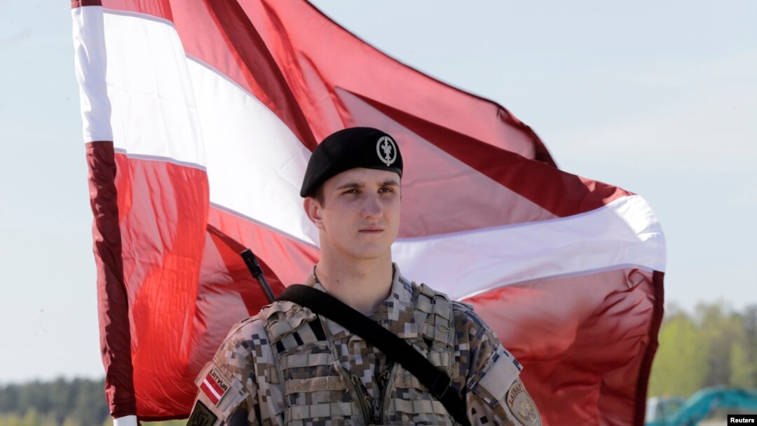 Seorang tentara Latvia memegang bendera nasional saat menanti pasukan AS yang akan datang untuk latihan militer, di bandara Riga, April 2014.