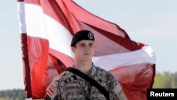 Seorang tentara Latvia memegang bendera nasional saat menanti pasukan AS yang akan datang untuk latihan militer, di bandara Riga, April 2014.