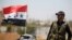 A Syrian army soldier stands next to a Syrian flag in Umm al-Mayazen, in the countryside of Daraa, Syria, July 10, 2018. 