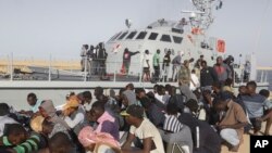 FILE - Rescued migrants are seated next to a coast guard boat in the city of Khoms, around 120 kilometers (75 miles) east of Tripoli, Libya, Oct. 1, 2019. 