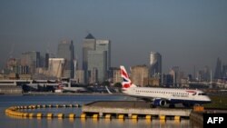 Un avión de British Airways espera en la pista con las torres y los edificios del distrito financiero de Canary Wharf, en el fondo, antes de despegar en el aeropuerto de London City. Foto de archivo.