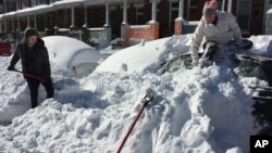 Anna Popp, 25, sits atop her snow-covered car on Guilford Avenue in Baltimore on Sunday, Jan. 24, 2016 after a storm dumped more than two feet of snow on to the city's streets.