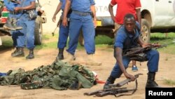 Burundian police officers collect a cache of weapons recovered from suspected fighters after clashes in the capital Bujumbura, Dec. 12, 2015.