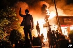 Protestors demonstrate outside of a burning fast food restaurant, May 29, 2020, in Minneapolis. Protests over the death of George Floyd, a black man who died in police custody Monday, broke out in Minneapolis for a third straight night.