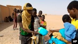 In this April 25, 2020 photo provided by IOM Niger, some of nearly 100 Nigeriens arrive in Assamaka, Niger, on foot from Algeria and now must be quarantined for two weeks at the remote Sahara border settlement.