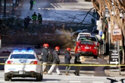 Investigators on Dec. 26, 2020, walk near the scene of an explosion in Nashville, Tenn. The explosion early Friday shattered windows, damaged buildings and left several people wounded.