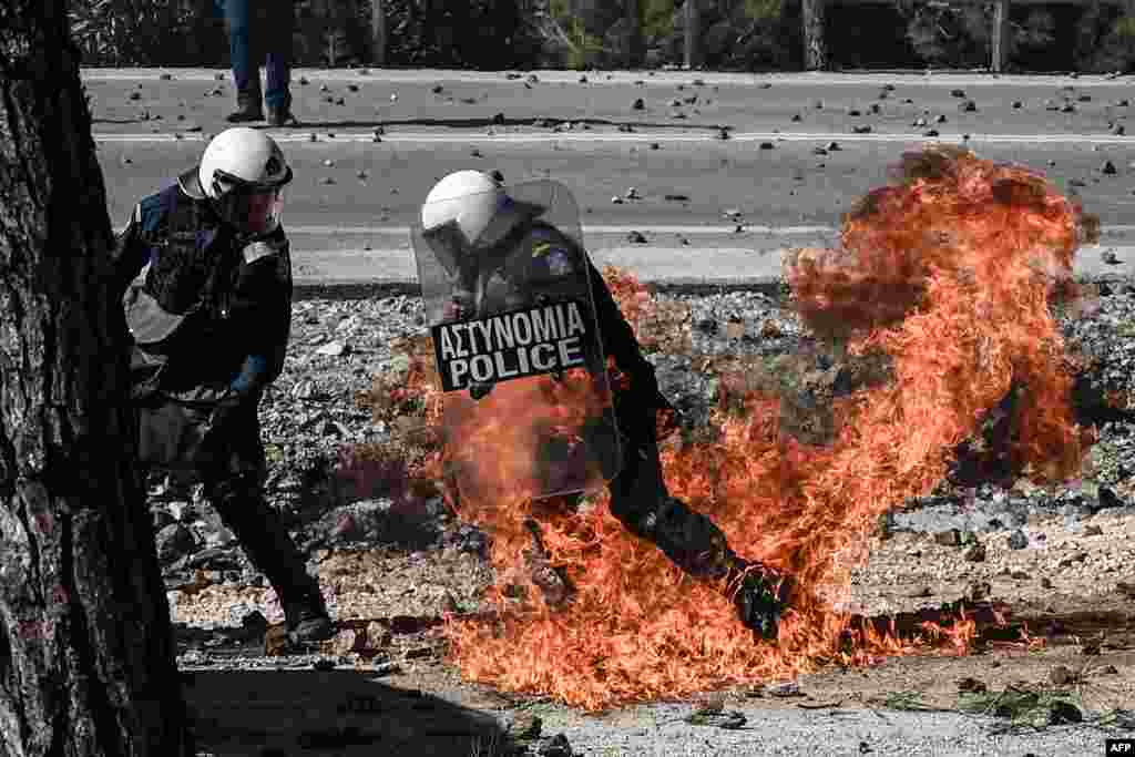 Greek anti-riot police officers try to move away from flames during clashes with demonstrators protesting against the construction of a new controversial migrant camp, near the town of Mantamados on the northeastern Aegean island of Lesbos.