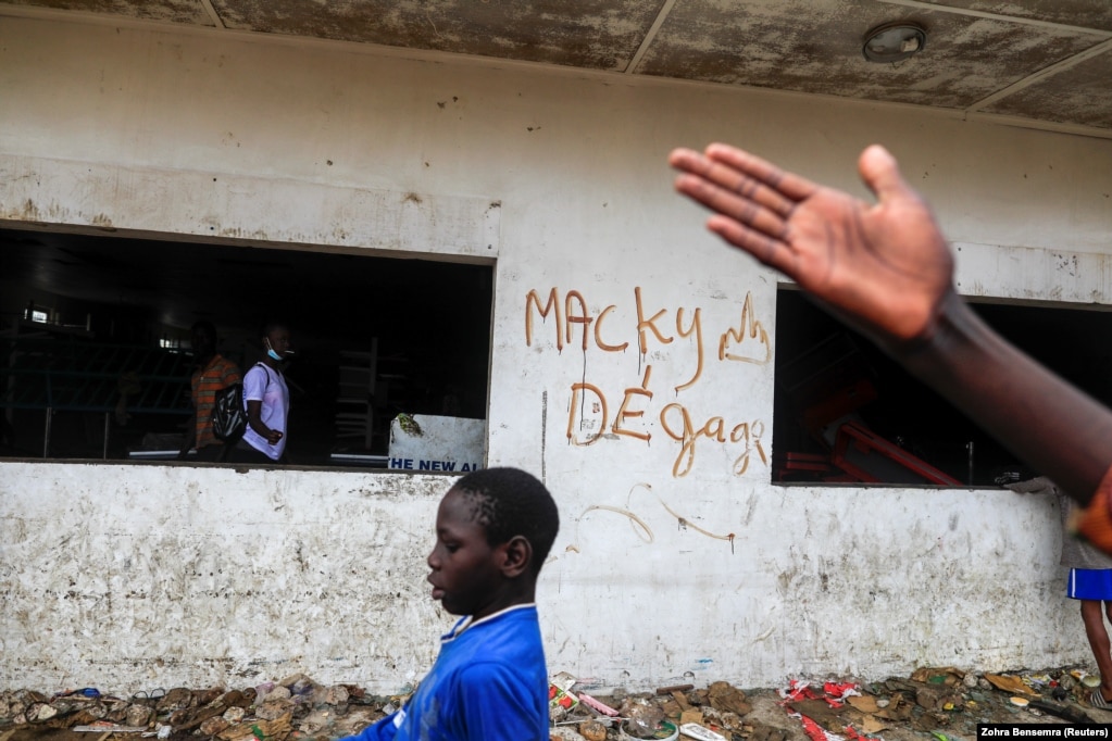 Un garçon passe devant un graffiti sur un mur d'un supermarché Auchan saccagé, sur lequel on peut lire "Macky dégage", à Dakar, Sénégal, le 5 mars 2021.