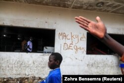 Un garçon passe devant un graffiti sur un mur d'un supermarché Auchan saccagé, sur lequel on peut lire "Macky dégage", à Dakar, Sénégal, le 5 mars 2021.