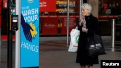 A woman smokes a cigarette as she stands by a sign encouraging people to wash their hands amid the outbreak of the coronavirus disease (COVID-19) in Belfast, Northern Ireland Jan. 2, 2021.