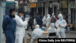 Pekerja media dengan APD membantu memindahkan warga ke fasilitas karantina menyusul infeksi baru COVID-19, di dekat Rumah Sakit Renji yang berafiliasi dengan Sekolah Kedokteran Universitas Jiao Tong Shanghai, di Shanghai, Cina. (Foto: Reuters)