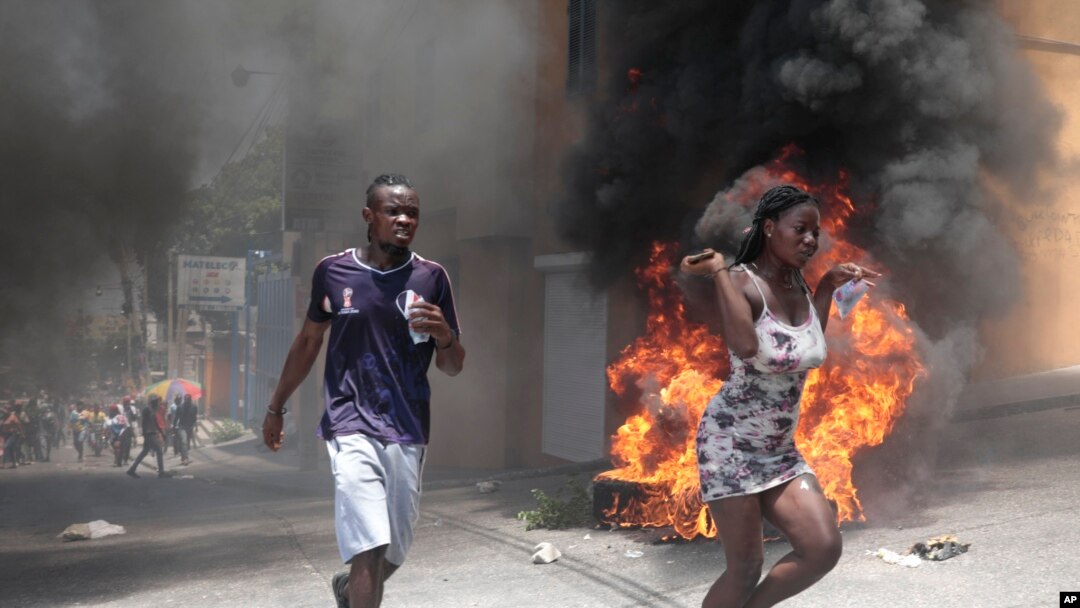 Manifestantes pasan corriendo junto a neumáticos incendiados durante una protesta contra la inseguridad en Puerto Príncipe, Haití, el 7 de agosto de 2023.