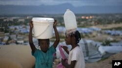 Haitian girls carry water to their family's tent at the Caradeux Camp in Port-au-Prince