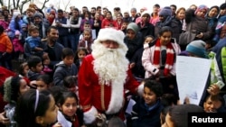 Enfants migrants reassembles autour d'un volontaire habille en peer Noel, rencontre facilitee par une organization humanitaire locale "Die Johanniter" au camp des refugies a Hanau, Germany, Dec. 24, 2015.REUTERS/Kai Pfaffenbach -