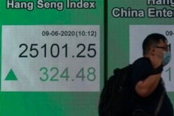 A man wearing a face mask walks past a bank electronic board showing the Hong Kong share index at Hong Kong Stock Exchange, June 9, 2020.