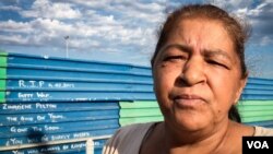 Maureen Johnstone stands at a street-side memorial to grandson Zinadene Pelton, 14, killed in gang crossfire in March 2017. Painted on the wall behind is the phrase 'the good die young.' (H. Adams FitzPatrick/VOA) 