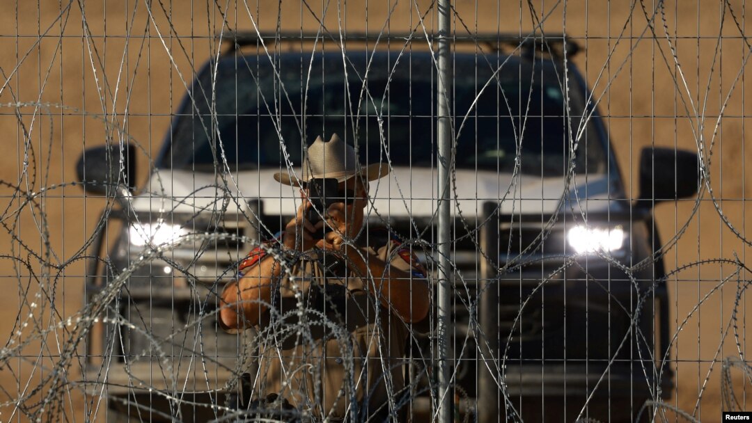 Un policía del Departamento de Seguridad Pública de Texas (DPS) fotografía con su teléfono celular cerca de una cerca de alambre de púas, usada para evitar que los migrantes crucen a EEUU, en la frontera con México, visto desde Ciudad Juárez, México, el 14 de agosto de 2024.