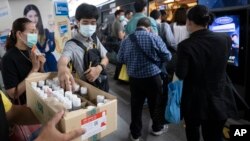 Commuters wearing face masks to protect themselves from new virus take clean gel for hands during a campaign for washing hands at the skytrain station in Bangkok, Thailand, Friday, Feb. 7, 2020. (AP Photo/Sakchai Lalit)