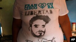 In this Oct. 16, 2015 photo, Maria Victoria Machado stands in her living room, wearing a T-shirt featuring a stencil art image of her son Danilo Maldonado, better known as El Sexto, in Havana, Cuba.