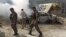 FILE - Afghan security forces walk past a burning car after a group of Taliban insurgents stormed a compound used by Afghanistan's intelligence agency in Kabul, Afghanistan, July 7, 2015.