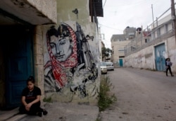 A Palestinian girl sits at the entrance of her family's house at Aida refugee camp in the West Bank, Tuesday, Oct. 6, 2015. Residents are short on supplies to protect themselves against the coronavirus.