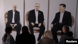 FILE - Visitors stand in front of an artwork depicting U.S. President Donald Trump, Russian President Vladimir Putin and Chinese President Xi Jinping at an exhibition called "Yalta 2.0" at an art gallery in Livadia park in Yalta, Crimea, Feb. 8, 2025. 