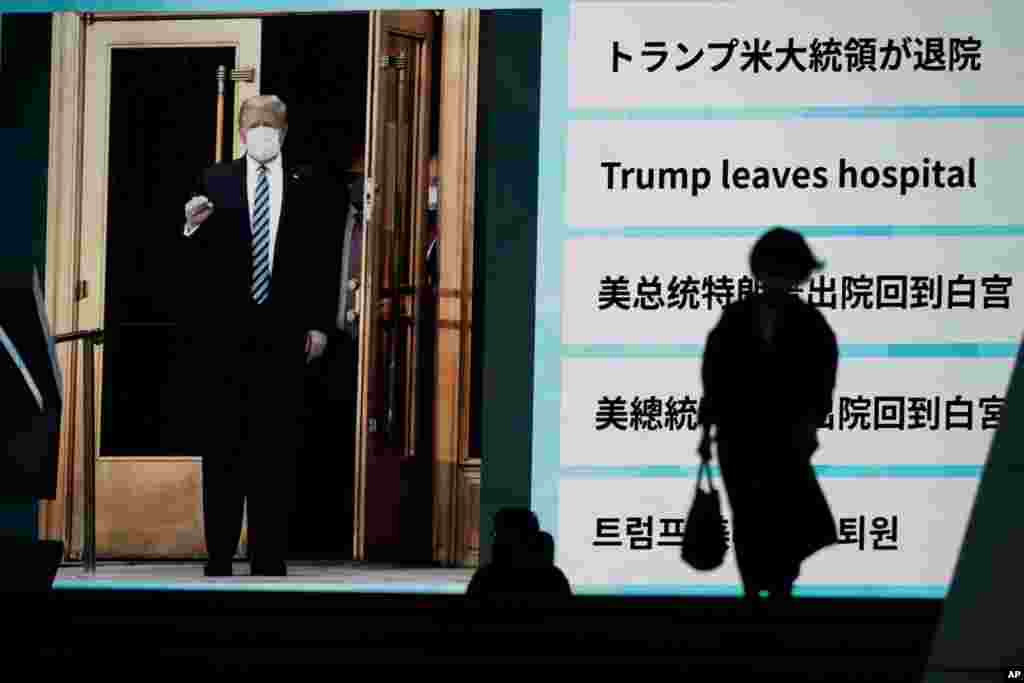 People walk past a screen in Tokyo, Japan, showing the news report that President Donald Trump has left a hospital to return to the White House after receiving treatments for COVID-19.