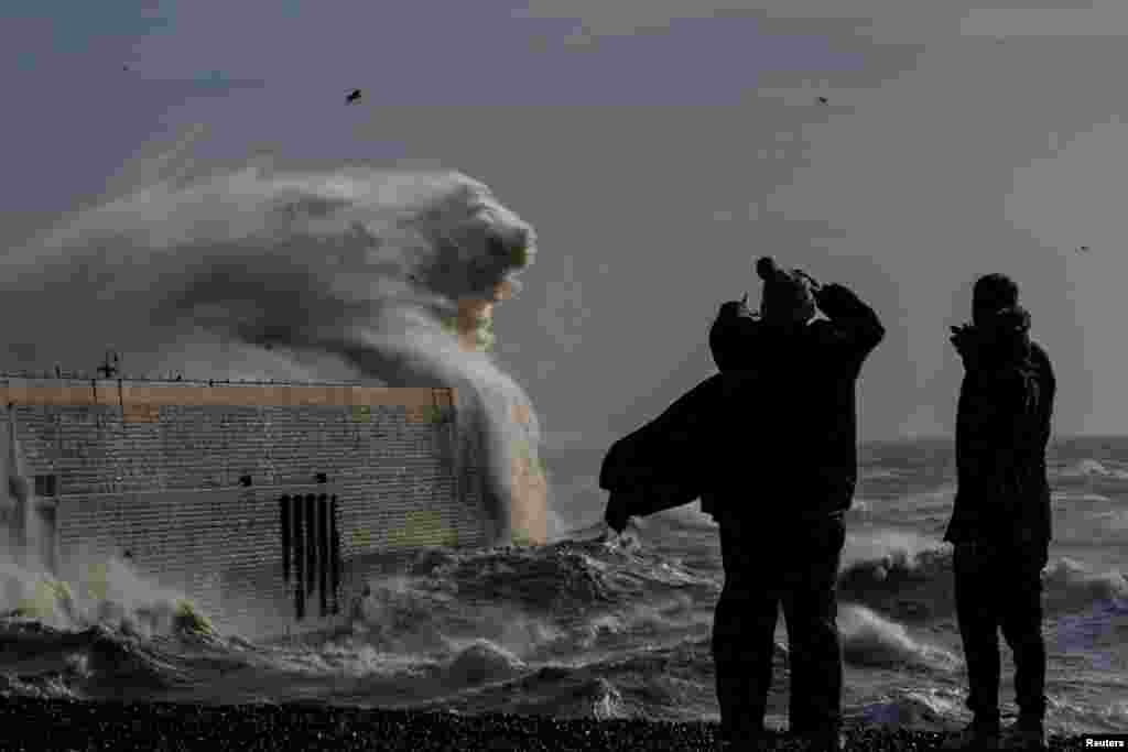 Locals look on as high winds from Storm Bert cause waves to crash over the harbor arm in Folkestone, Britain.