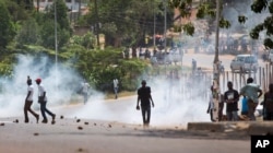 FILE - A voter holds a rock as riot police fire tear gas at a crowd of angry voters outside a polling station where voting material for the presidential election never arrived, at a polling station in Ggaba, Uganda, Feb. 18, 2016.