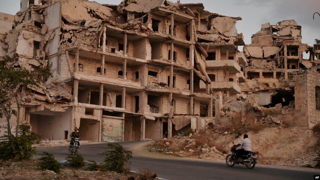 FILE - People on motorcycles ride past buildings destroyed during the fighting in the northern town of Ariha, in Idlib province, Syria. Ariha is one of five main towns in Idlib province and the last place to fall to rebel control in 2015, Sept. 20, 2018 photo. 