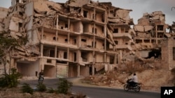 FILE - People on motorcycles ride past buildings destroyed during the fighting in the northern town of Ariha, in Idlib province, Syria. Ariha is one of five main towns in Idlib province and the last place to fall to rebel control in 2015, Sept. 20, 2018 photo. 