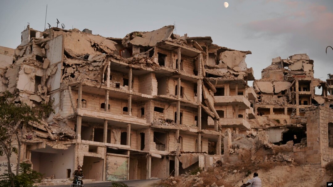 FILE - In this Sept. 20, 2018 photo, motor cycles ride past buildings destroyed during the fighting in the northern town of Ariha, in Idlib province, Syria. Ariha is one of five main towns in Idlib province and the last place to fall to rebel control in 2015. 