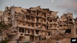 FILE - In this Sept. 20, 2018 photo, motor cycles ride past buildings destroyed during the fighting in the northern town of Ariha, in Idlib province, Syria. Ariha is one of five main towns in Idlib province and the last place to fall to rebel control in 2015. 