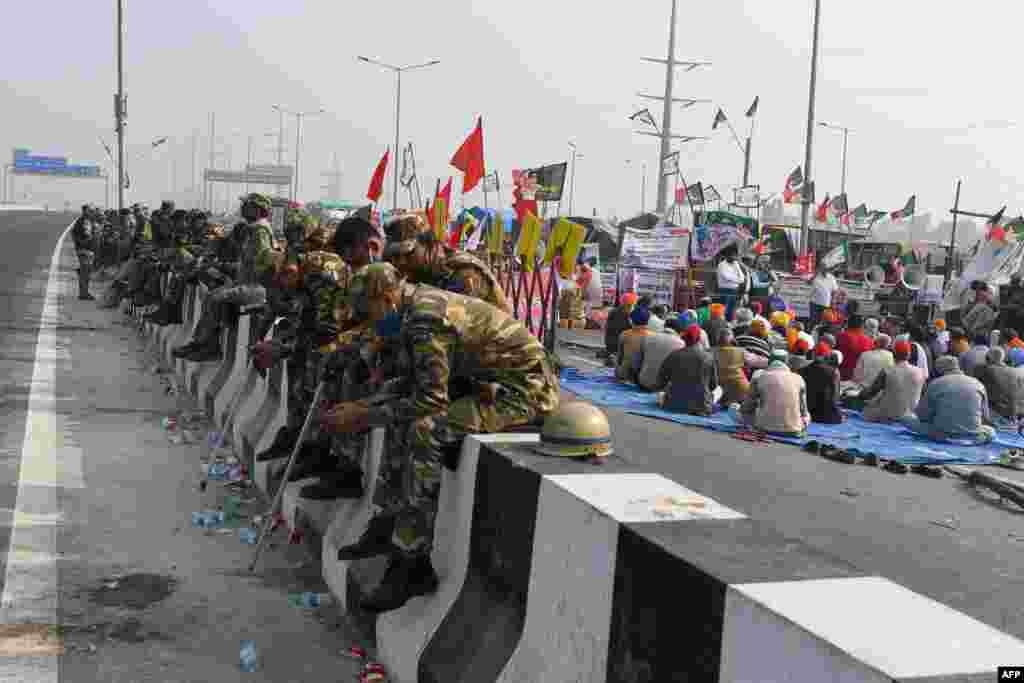 Security personnel sit next to farmers as they continue a demonstration to protest against the recent agricultural reforms at the Delhi-Uttar Pradesh state border in Ghazipur, India.