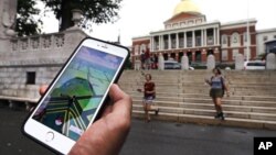 Seorang pemain Pokemon Go melihat ponselnya sambil berjalan melalui di luar gedung pemerintah di Boston, Massachusetts (18/7). (AP/Charles Krupa)