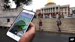 A Pokemon Go player consults his phone while walking through the Boston Common outside the Massachusetts Statehouse. The game has introduced players to some aspects of history they otherwise might have missed.