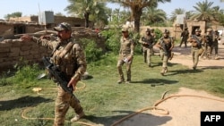 FILE - Iraq’s rapid response forces storm a house in the Tarmiyah district, north of Baghdad, searching for wanted Islamic State group suspects, July 21, 2019. Iraq declared victory against IS in 2017, but the group continues to attack with sleeper cells.