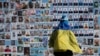 Seorang perempuan yang menyampirkan bendera Ukraina di pundaknya berdiri di samping Tembok Kenangan Para Pembela Ukraina yang tewas dalam Perang Rusia-Ukraina, pdi Kyiv, Ukraina, Selasa, 14 Maret 2023. (Foto: AP/Andrew Kravchenko)