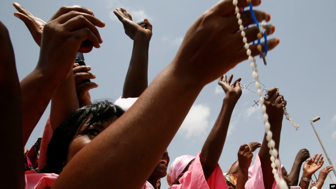 FILE - Women from a Catholic society wave rosary beads as they watch the convoy of Pope Benedict XVI pass on the way to a meeting between the pope and Cameroonian bishops, in Yaounde, March 18, 2009. 