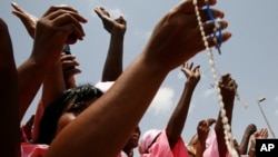 FILE - Women from a Catholic society wave rosary beads as they watch the convoy of Pope Benedict XVI pass on the way to a meeting between the pope and Cameroonian bishops, in Yaounde, March 18, 2009. 