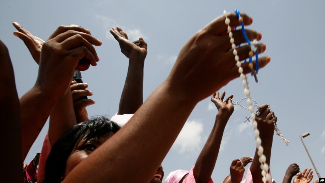 FILE - Women from a Catholic society wave rosary beads as they watch the convoy of Pope Benedict XVI pass on the way to a meeting between the pope and Cameroonian bishops, in Yaounde, March 18, 2009. 