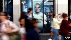 ARCHIVO - Los peatones pasan junto a un gran cartel del delantero de fútbol francés del Real Madrid, Kylian Mbappé, exhibido en una de las tiendas oficiales del Real Madrid en el centro de Madrid, el 13 de septiembre de 2024.