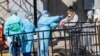 A member of the Brooklyn Hospital Center helps a person who was just tested for COVID-19 put an object in a biohazard bag, March 26, 2020, in New York.