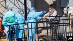 A member of the Brooklyn Hospital Center helps a person who was just tested for COVID-19 put an object in a biohazard bag, March 26, 2020, in New York.