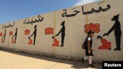 FILE - An Iraqi student walks past a school wall covered with drawings showing how Islamic State militants executed their prisoners in Mosul, Iraq, April 30, 2018.