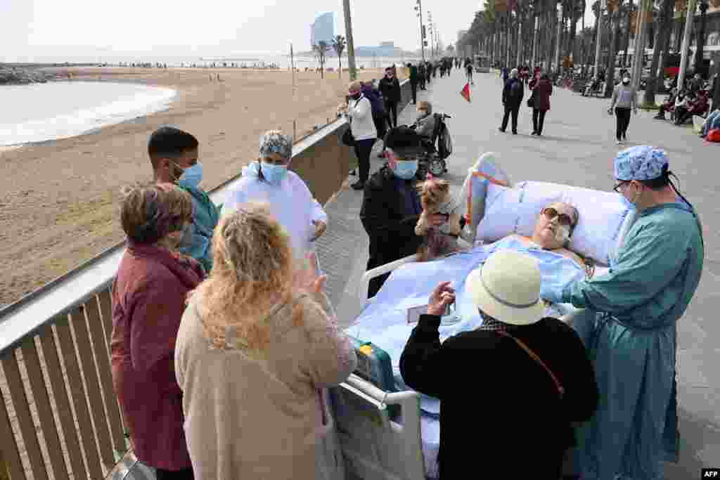 Friends, neighbors and medical personnel surround COVID-19 patient, Marta Pascual, 72, as she gets some fresh air at the Barceloneta beach esplanade outside Hospital del Mar in Barcelona, Spain.