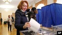 ແມ່​ຍິງ​ຄົນ​ນຶ່ງ​ອຸ້ມ​ສັດ​ລ້ຽງ​ຂອງ​ລາວ ແລະ ປ່ອນ​ບົດ​ຄະ​ແນນ​ສຽງ ຢູ່​ສະ​ຖານ​ທີ່​ເລືອກ​ຕັ້ງ ໃນ​ລະ​ຫວ່າງ​ການ ເລືອກ​ຕັ້ງ​ປະ​ທາ​ນາ​ທິ​ບໍ​ດີ, ນະ​ຄອນຫຼວງ ກຽບ, ຢູ​ເຄ​ຣນ. 31 ມີ​ນາ, 2019.