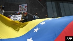Activistas sostienen un cartel que dice “vacunas para todos” y una bandera gigante venezolana durante una protesta para exigir que todos los trabajadores de la salud sean vacunados contra el COVID-19, en Caracas, el 17 de abril de 2021.