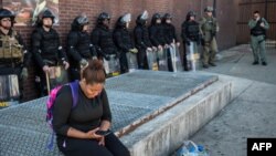 A woman checks her phone while police officers monitor the situation near a pharmacy that was looted and burned by rioters on Monday after the funeral of Freddie Gray, on April 29, 2015, in Baltimore, Maryland. 